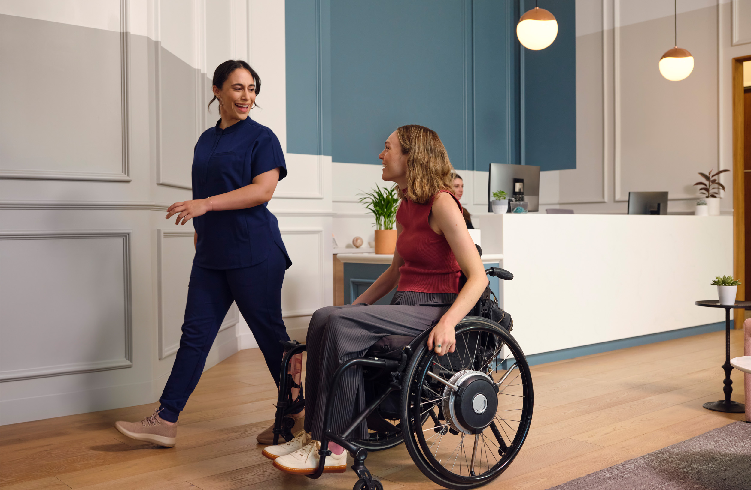 Healthcare Professional Walks Beside a Smiling Woman in a Wheelchair in a Clinic